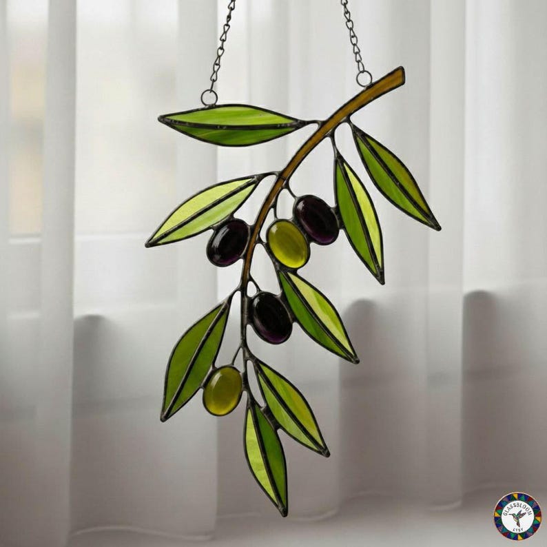May include: Stained glass olive branch with green leaves and black and green olives. The branch is brown and hangs from a chain. The glass is outlined in black.