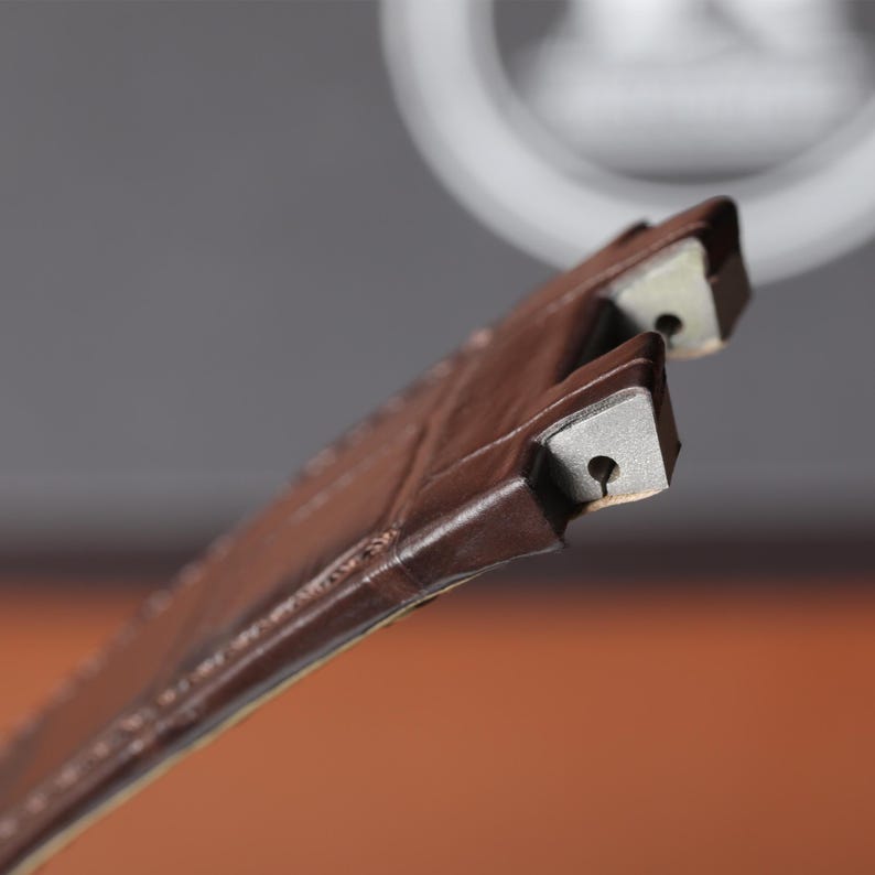 Puede incluir: Primer plano de dos correas de reloj de cuero marr&oacute;n con cierres met&aacute;licos. Las correas est&aacute;n cosidas y tienen un aspecto texturizado. Los cierres met&aacute;licos tienen un peque&ntilde;o agujero en el centro.