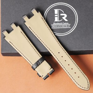 Op de afbeelding: Tweedelig horlogebandje van beige leer met zwarte stiksels. De band heeft een zwarte leren lus en een roestvrijstalen gesp. De tekst "Handmade Custom DRWATCHSTRAP" is zichtbaar op de verpakking.