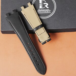 Op de afbeelding: Twee horlogebandjes. E&eacute;n is zwart, de andere is beige met een zwart accent. De zwarte band heeft verschillende gaten voor aanpassing. De beige band heeft een zwarte leren lus. De doos heeft de tekst "Handmade Custom DRWATCHSTRAP".