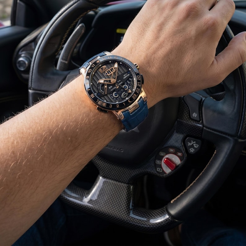 Puede incluir: Un reloj de lujo con caja dorada, esfera negra y correa de cuero azul. El reloj presenta m&uacute;ltiples subesferas y una esfera detallada. El reloj se lleva en la mu&ntilde;eca.