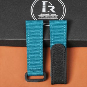 Puede incluir: Correas de reloj de color turquesa con herrajes y costuras negras. Las correas están hechas de una tela duradera y se muestran sobre un fondo oscuro. La marca "DRWATCHSTRAP" es visible.