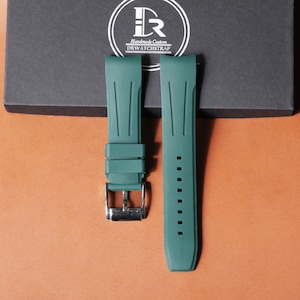 Puede incluir: Dos correas de reloj color turquesa con hebilla plateada y orificios de ajuste. Las correas se muestran sobre una superficie marrón con una caja gris oscura en el fondo. La caja tiene un logotipo blanco con el texto "Handmade Custom DRWATCHSTRAP".
