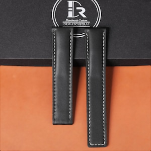 Könnte beinhalten: Zwei schwarze Leder-Uhrenarmbänder mit weißen Nähten werden vor einem braunen und schwarzen Hintergrund gezeigt. Die Armbänder stammen von DRWATCHSTRAP, einer handgefertigten Custom-Marke. Die Armbänder sind rechteckig mit abgerundeten Enden.