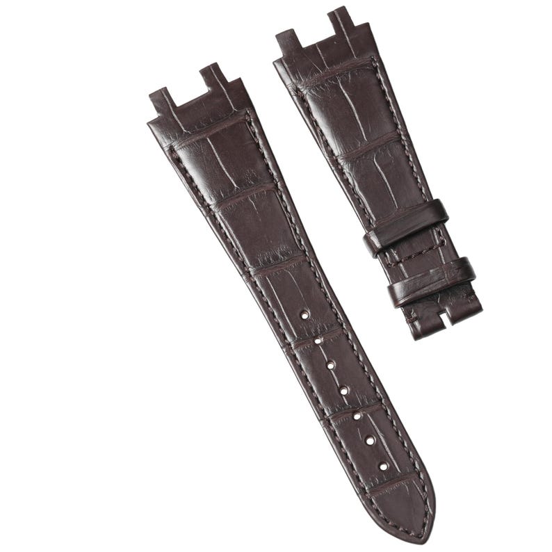 Puede incluir: Dos correas de reloj marr&oacute;n oscuro con textura de piel de cocodrilo. Las correas tienen un dise&ntilde;o rectangular en la parte superior para sujetarlas a la caja del reloj y varios agujeros para la hebilla. Las correas son de cuero.