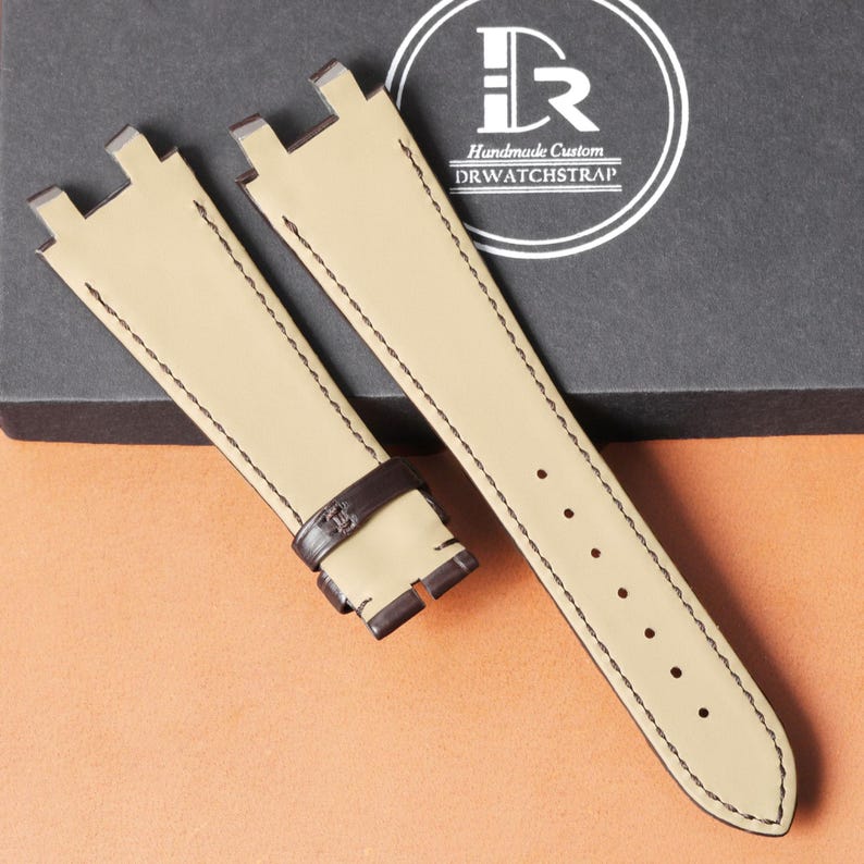 Puede incluir: Dos correas de reloj beige con detalles y costuras marr&oacute;n oscuro. Las correas son de cuero y tienen forma rectangular con hebilla. El texto "Handmade Custom DRWATCHSTRAP" es visible en el fondo.