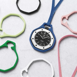 May include: A blue watch with a black and white face and a blue strap, surrounded by various colored watch bands in black, green, pink, and white. The watch face has silver hands and markers.