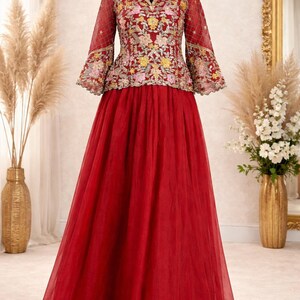 May include: A floor-length red dress featuring a sheer overlay skirt and a fitted bodice with three-quarter length bell sleeves. The bodice is adorned with intricate floral embroidery in shades of pink, yellow, and gold with metallic thread accents.