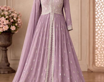 Peut inclure: Une robe longue couleur lavande avec un décolleté en V, des manches longues et une jupe fendue sur le devant. Le corsage et l'ourlet sont ornés de broderies argentées complexes. Une écharpe dupatta lavande assortie est drapée autour du cou.