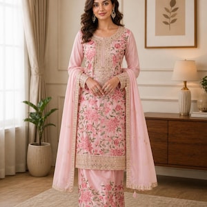 May include: A light pink three-piece outfit consisting of a long-sleeved tunic, a matching skirt, and a sheer dupatta. The tunic and skirt feature intricate floral embroidery in shades of pink and green, accented with gold metallic trim and sequins.