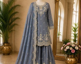 Peut inclure: Un ensemble trois pièces bleu ardoise composé d'une tunique à manches longues, d'un pantalon large et d'un dupatta assorti. Les vêtements sont ornés de broderies argentées complexes sur les encolures, les ourlets et les bords festonnés du dupatta.