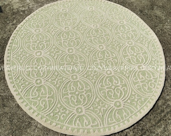 May include: A round, light green rug with a cream-colored border. The rug features a repeating pattern of stylized floral and geometric shapes. The rug is made of a soft, textured material and is suitable for indoor use.