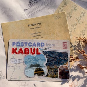 May include: A postcard from Kabul, Afghanistan, with a map and images of the city, including a yellow taxi and snowy mountains. The postcard is layered with other paper items, including a sketch of a building and the text "Studio +93".