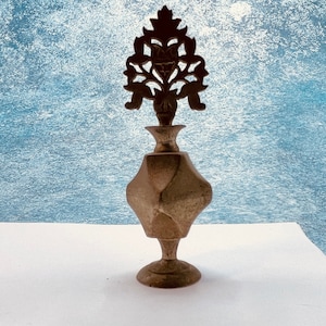 May include: A gold metal perfume bottle with an ornate, floral-shaped stopper. The bottle has a faceted, geometric design.