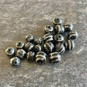 May include: A collection of black and silver beads with intricate designs. The beads are round and have a smooth, polished finish.