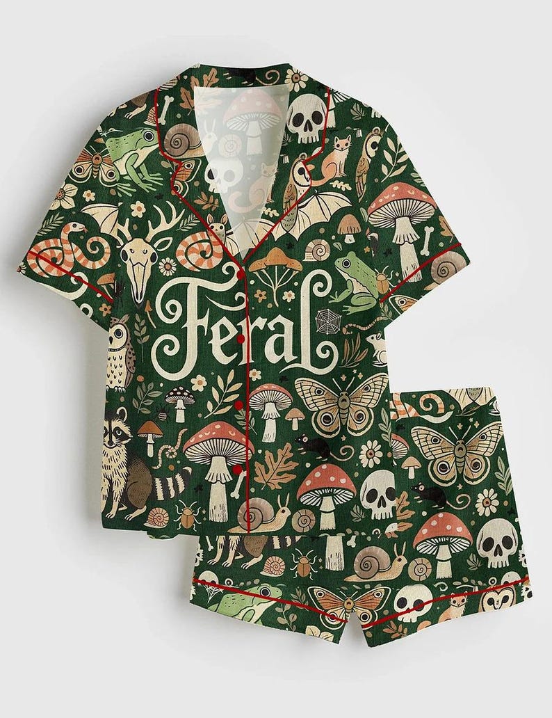 Op de afbeelding: Groene pyjamaset met een grillig patroon van paddenstoelen, schedels, vlinders en bosdieren. De shirt en short hebben rode biezen en het woord "Feral" in een decoratief lettertype.