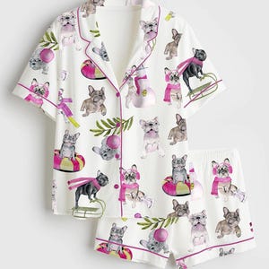 May include: White pajama set with a repeating pattern of French bulldogs in various poses. The short-sleeved top and shorts are trimmed with pink piping. The bulldogs are wearing scarves and hats.