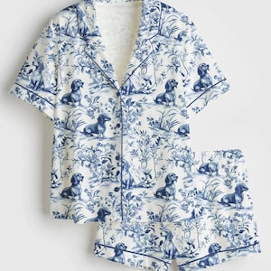 Puede incluir: Conjunto de pijama blanco con un estampado azul toile de Jouy con perros salchicha y elementos florales. La parte superior de manga corta y los pantalones cortos a juego tienen ribetes azules. La tela tiene un aspecto suave y c&oacute;modo.