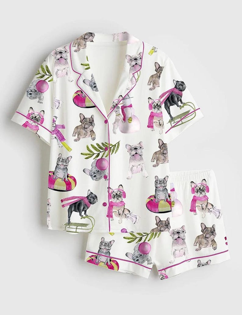 May include: White pajama set with a repeating pattern of French bulldogs in winter scenes. The short-sleeved top and shorts are trimmed in pink. The bulldogs are wearing scarves and hats.
