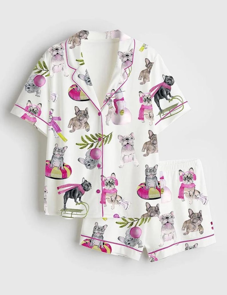 May include: White pajama set with a repeating pattern of French bulldogs in various poses, some wearing scarves and hats. The set includes a short-sleeved button-up shirt and matching shorts, both trimmed with pink piping.