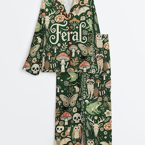 Op de afbeelding: Groene pyjamaset met een grillige bosprint met paddenstoelen, vlinders en bosdieren. Het woord "Feral" staat op de top gedrukt. De set heeft rode bies.