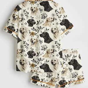 May include: Cream-colored pajama set featuring a repeating pattern of black and golden Labrador Retriever faces, roses, and foliage. The short-sleeved top and shorts have orange trim.