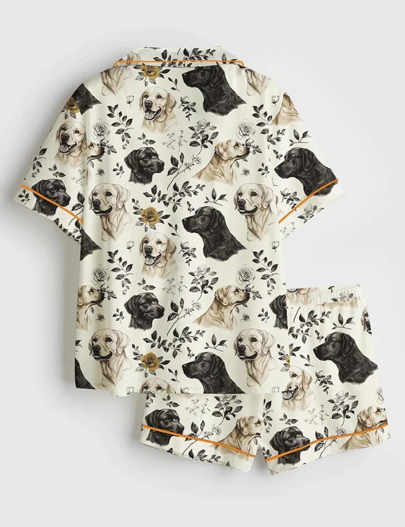 May include: Cream-colored pajama set featuring a repeating pattern of black and golden Labrador Retriever faces, roses, and foliage. The short-sleeved top and shorts have orange trim.