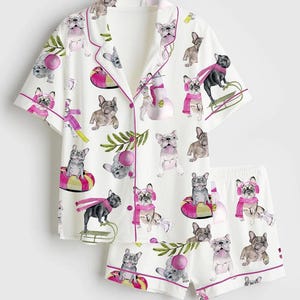 May include: White pajama set with a repeating pattern of French bulldogs in various poses, some wearing scarves and hats. The set includes a short-sleeved top with pink trim and matching shorts. The bulldogs are in different colors.