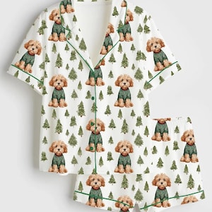 May include: White pajama set with a repeating pattern of brown dogs wearing green sweaters and green Christmas trees. The set includes a short-sleeved button-up shirt and matching shorts, both trimmed with green piping.