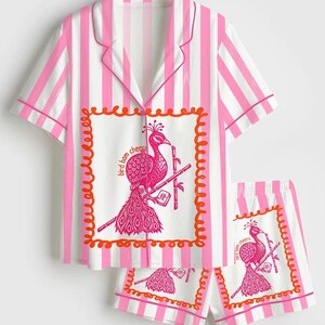 May include: Pink and white striped pajama set. The top has short sleeves and a collar, with a peacock graphic on the front. The shorts have a matching peacock graphic. The text "bird bam cheers" is printed on the top and shorts.