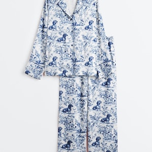Puede incluir: Conjunto de pijama de dos piezas con un estampado de toile de Jouy azul y blanco con perros salchicha y elementos florales. La parte superior de manga larga tiene botones y los pantalones son de corte holgado.