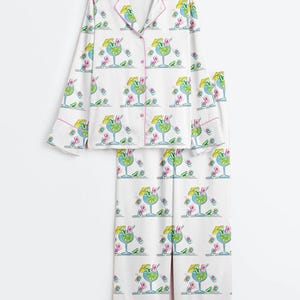 Puede incluir: Conjunto de pijama blanco con estampado de c&oacute;cteles. La parte superior de manga larga y los pantalones presentan un patr&oacute;n repetido de c&oacute;cteles azules con sombrillas amarillas y detalles en rosa. El conjunto tiene ribetes rosas.