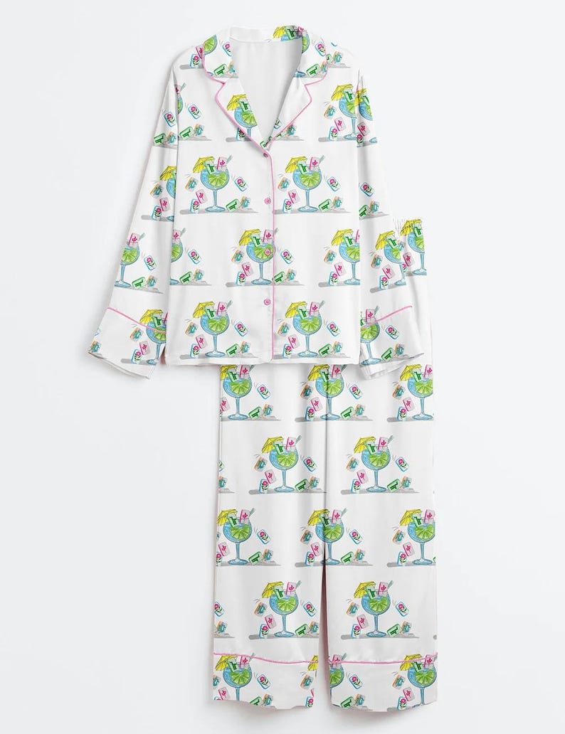 Puede incluir: Conjunto de pijama blanco con estampado de c&oacute;cteles. La parte superior de manga larga y los pantalones presentan un patr&oacute;n repetido de c&oacute;cteles azules con sombrillas amarillas y detalles en rosa. El conjunto tiene ribetes rosas.