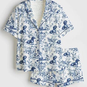 Puede incluir: Conjunto de pijama blanco con estampado de perros salchicha y flores azules. La parte superior de manga corta tiene cuello con solapas y cierre de botones. Los pantalones cortos tienen cintura el&aacute;stica y ribete azul. El conjunto es de tejido suave y ligero.