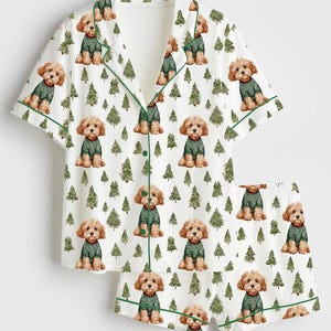 May include: White pajama set with a repeating pattern of brown dogs wearing green sweaters and green Christmas trees. The short-sleeved top and shorts have green trim.