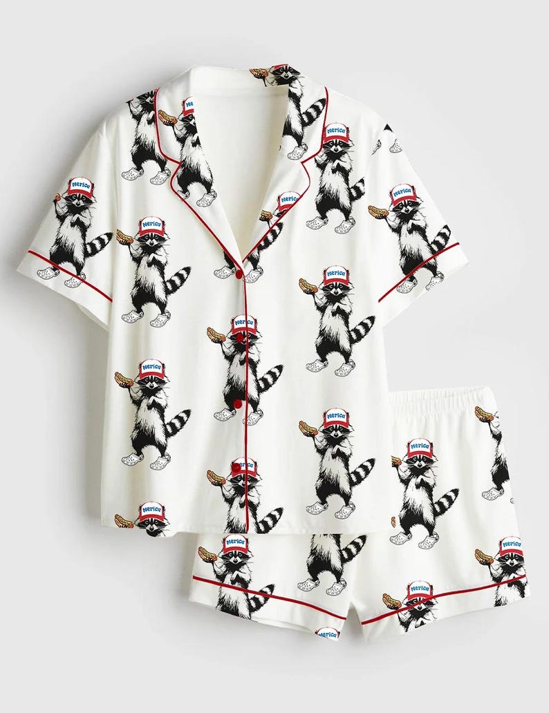 Op de afbeelding: Witte pyjamaset met een herhaald patroon van wasberen met rode hoeden en eten. De top met korte mouwen en de shorts hebben rode biezen. De wasberen zijn zwart, wit en grijs.
