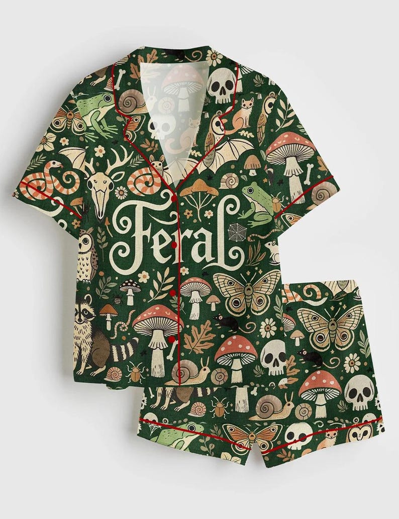 Op de afbeelding: Groene pyjamaset met een grillig bospatroon met paddenstoelen, schedels, vlinders en bosdieren. De set bevat een overhemd met knopen en een korte broek, beide afgezet met rode biezen. Het woord "Feral" staat op het shirt.