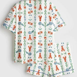 May include: White pajama set with a lobster and floral pattern. The short-sleeved top and shorts feature a repeating design of red lobsters, blue flowers, and green foliage, outlined with blue trim.