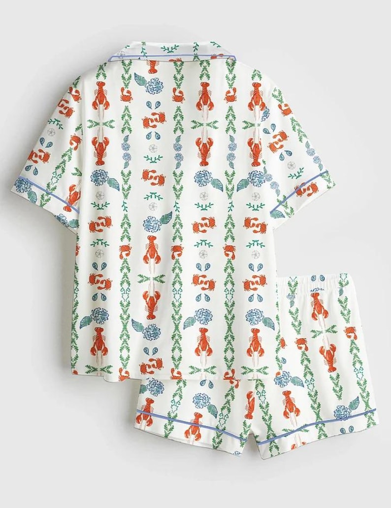 May include: White pajama set with a lobster and floral pattern. The short-sleeved top and shorts feature a repeating design of red lobsters, blue flowers, and green foliage, outlined with blue trim.