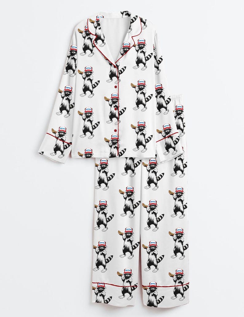 Op de afbeelding: Witte pyjamaset met een herhalend patroon van wasberen met honkbalpetten en knuppels. De top met lange mouwen heeft rode biezen en knopen. De pyjamabroek heeft ook rode afwerking. Een leuke en speelse nachtkledingset.