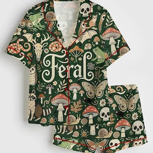 Op de afbeelding: Groene pyjamaset met een grillig bospatroon met paddenstoelen, schedels, vlinders en bosdieren. De set bevat een overhemd met knopen en een korte broek, afgezet met rode biezen. Het woord "Feral" staat op het shirt.