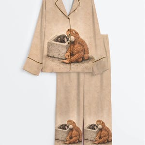 May include: Beige pajama set featuring a brown bear and a black monkey illustration. The long-sleeved top has a notched collar and button closure. The pants have a matching illustration. Brown piping trims the edges of the set.