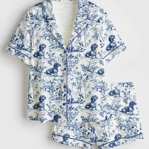 Puede incluir: Conjunto de pijama blanco con un estampado azul toile de Jouy con perros salchicha y elementos florales. La parte superior de manga corta y los pantalones cortos a juego tienen ribetes azules. La tela tiene un aspecto suave y c&oacute;modo.