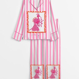 May include: Pink and white striped pajama set. The top has a collared neckline and long sleeves. The set features a pink peacock graphic with the text "bird bom cheers" in a decorative frame. The pants have the same graphic.