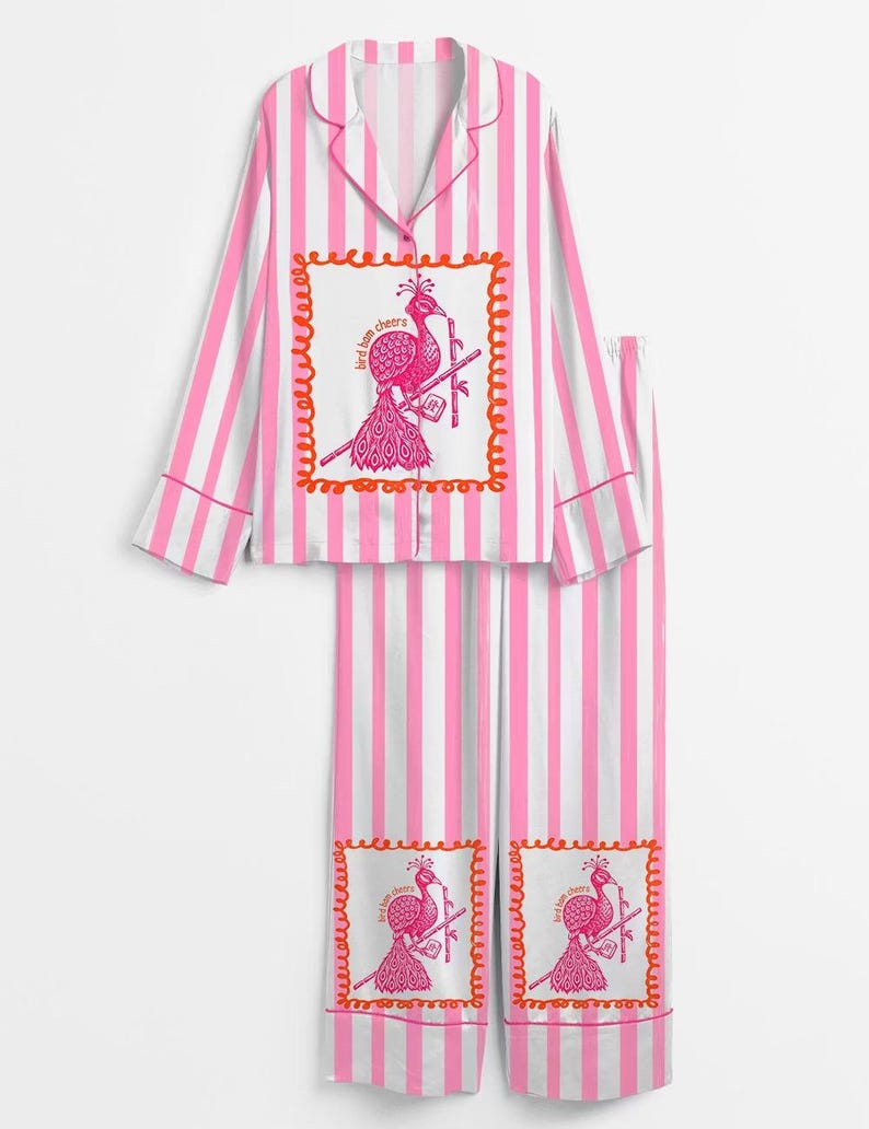 May include: Pink and white striped pajama set. The top has a collared neckline and long sleeves. The set features a pink peacock graphic with the text "bird bom cheers" in a decorative frame. The pants have the same graphic.