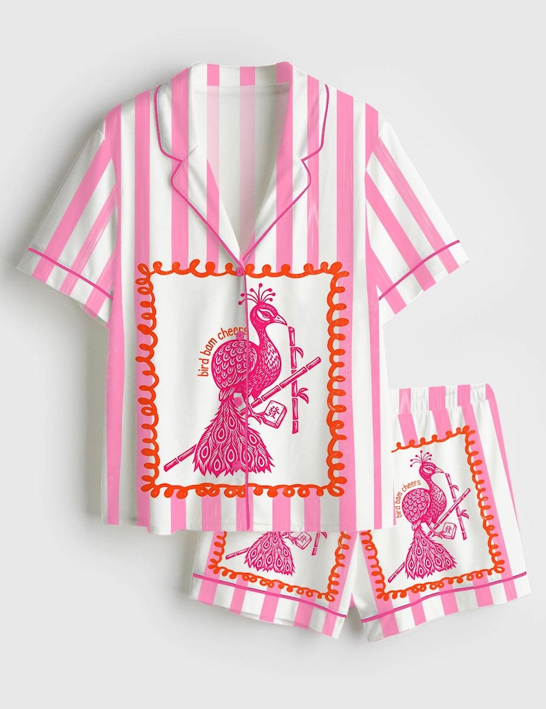 May include: Pink and white striped pajama set. The short-sleeved top and shorts feature a peacock graphic with the text "bird bam cheers" inside a decorative frame. The set has pink trim.