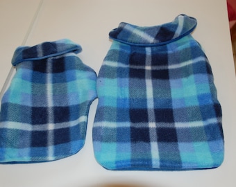 May include: Two blue plaid fleece hot water bottle covers. The covers are in shades of blue, with a plaid pattern. One cover is smaller than the other. Both have a rolled collar.