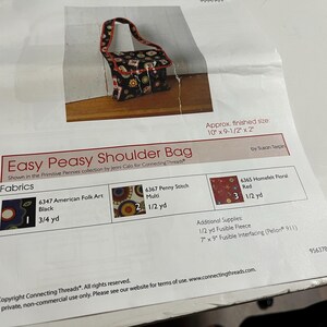May include: A sewing pattern for an Easy Peasy Shoulder Bag, featuring a black and white fabric with red accents. The pattern includes instructions for cutting and sewing the bag, as well as a list of required fabrics and supplies. The finished bag measures 10 inches by 9 1/2 inches by 2 inches.