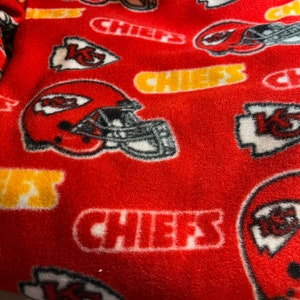 K&ouml;nnte beinhalten: Roter Fleece-Stoff mit einem sich wiederholenden Muster aus wei&szlig;em "Chiefs"-Text, einem wei&szlig;en Pfeil mit "K.C." darin und einem wei&szlig;en Footballhelm mit schwarzen Details.