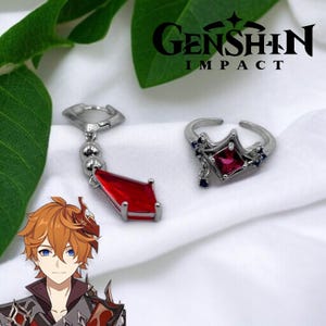 May include: Silver-toned ring and earring set. The ring features a red square gem and blue accents. The earring has a red, rectangular gem pendant. The image includes the text "Genshin Impact".